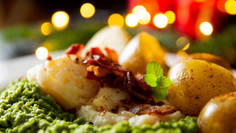 A plate of lufefisk topped with bacon and served with potatoes and peas.