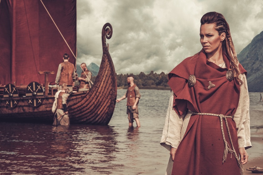 Viking woman standing near Drakkar on seashore