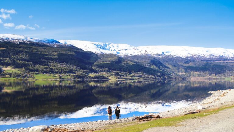 Two hikers admiring the mountain and lake scenery in Voss, Norway.
