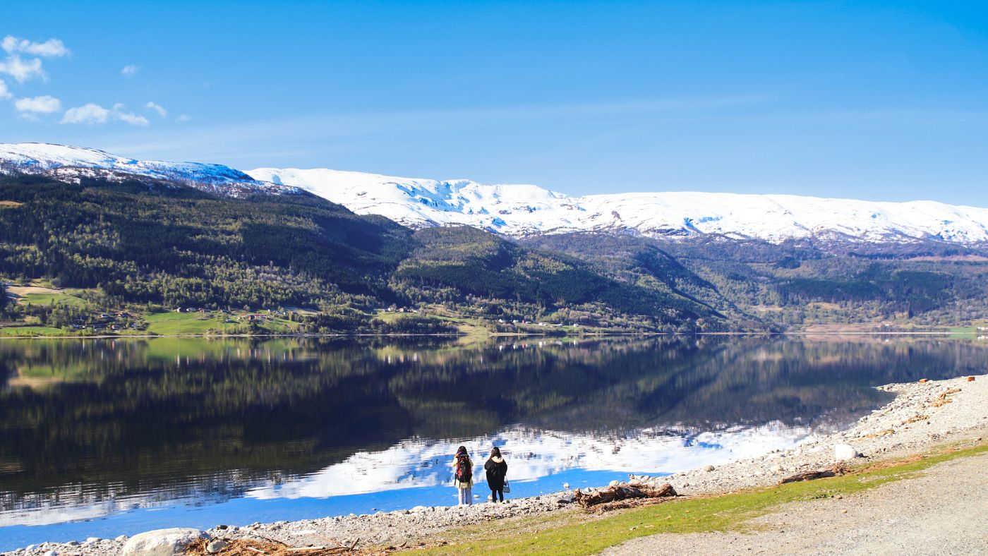Two hikers admiring the mountain and lake scenery in Voss, Norway.
