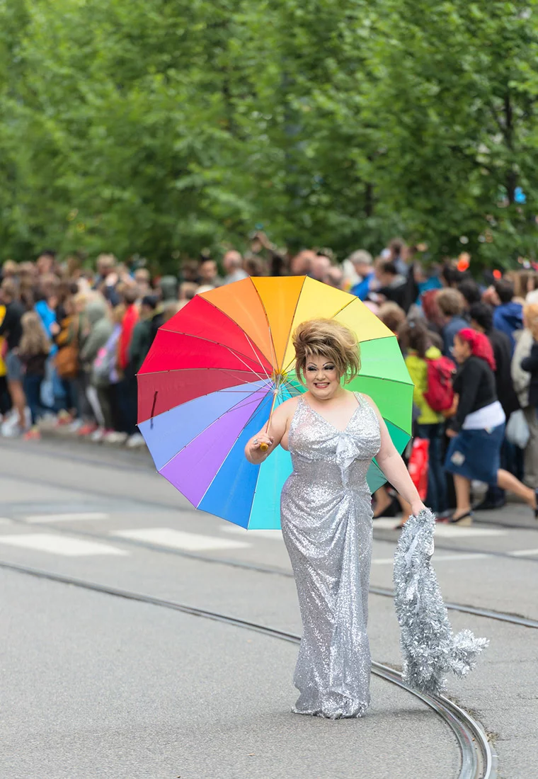 A happy participant in the Oslo Pride parade holding a rainbow umbrella
