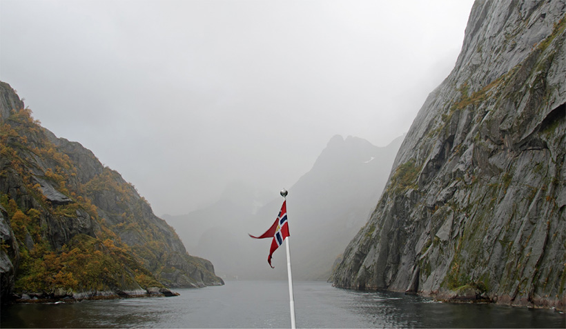 A boat with a Norwegian flag sailing into Norway's Trollfjord