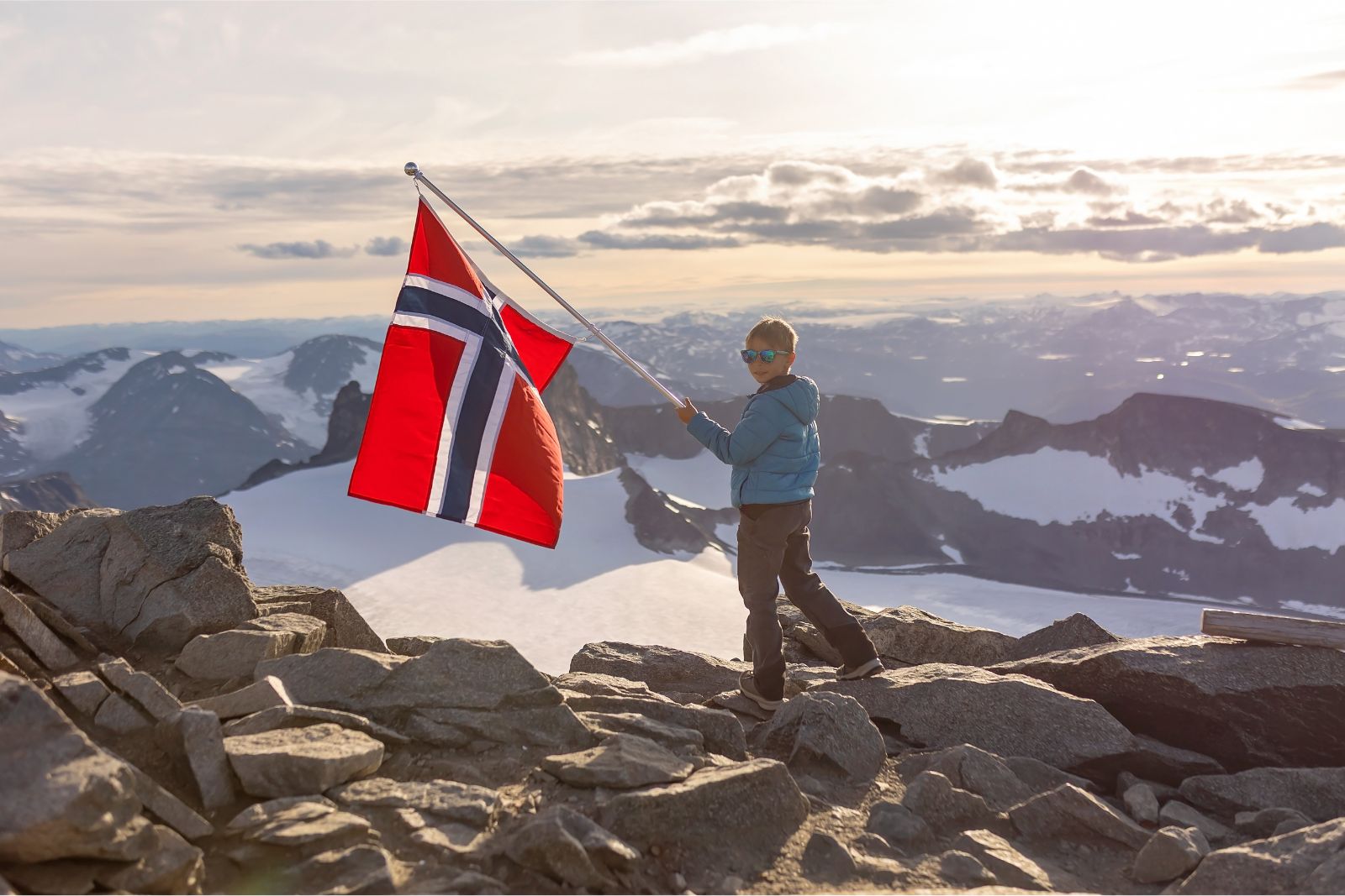 Young hiker waving the flag of Norway on Galdhøppigen mountain.