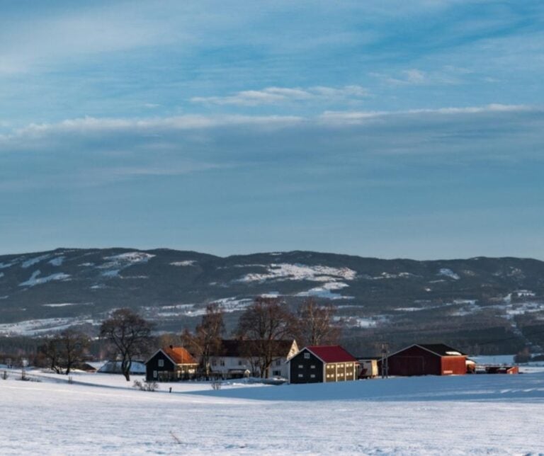 Winter landscape with wooden houses during calm winter morning with forest and hills in the background near Gjøvik