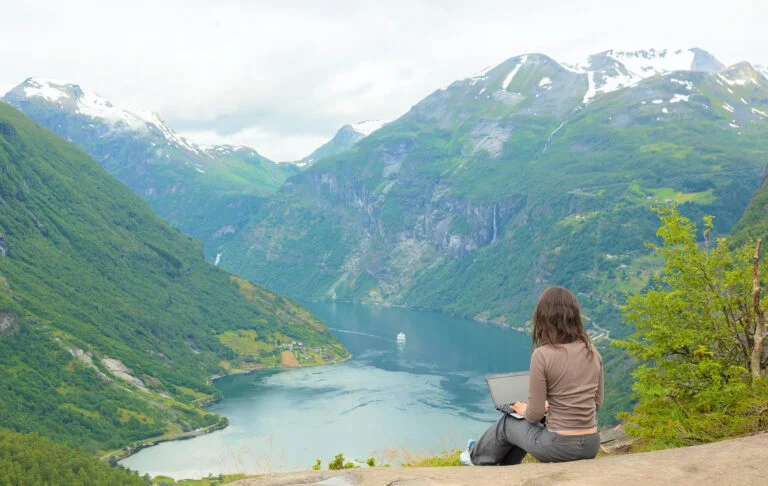 Girl on a laptop by a fjord.