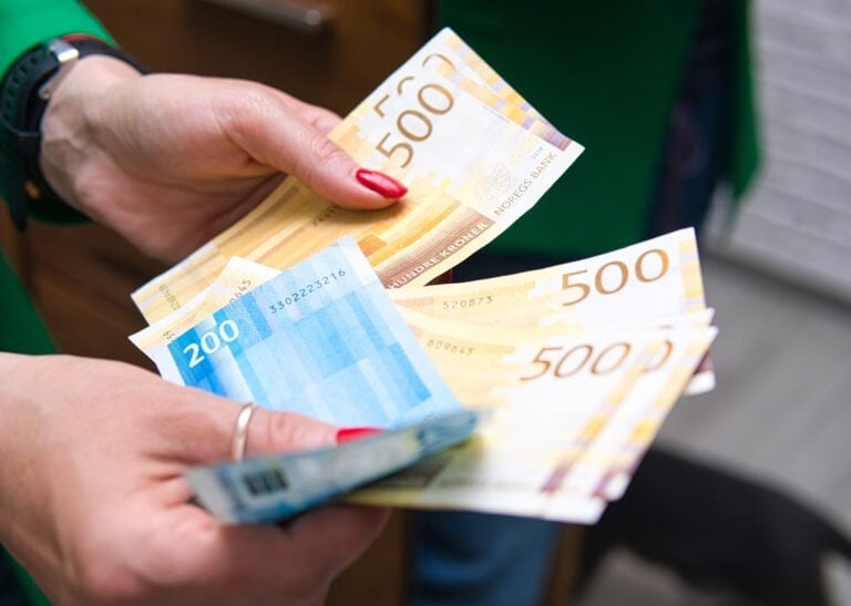Norwegian krone banknotes in a person's hand.