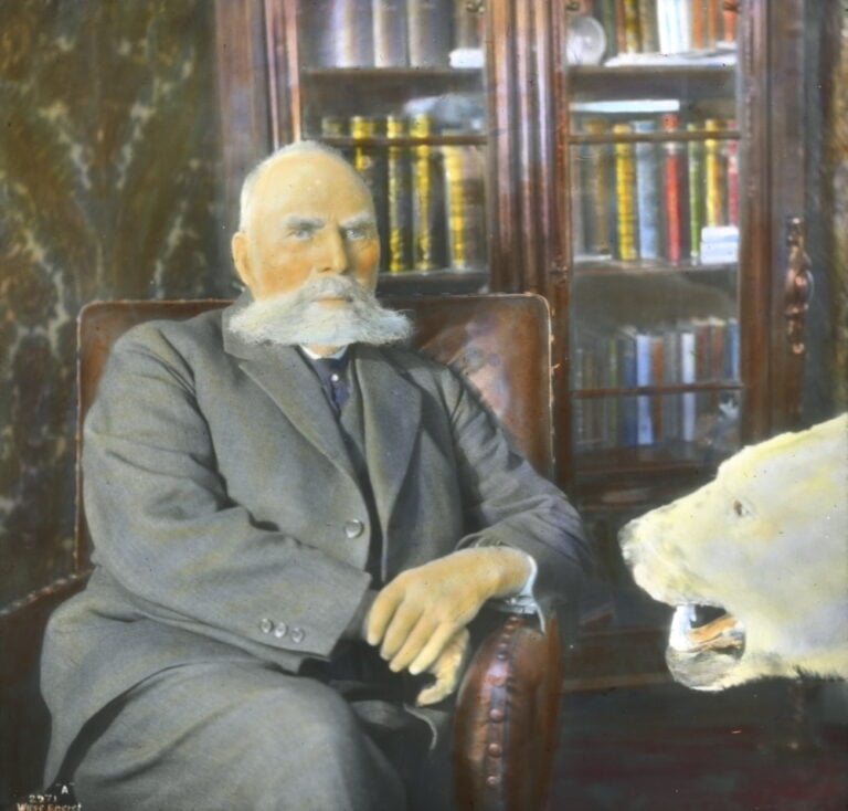 Hand-coloured slide of Otto Sverdrup with  a stuffed polar bear in the foreground. From the year 1928. Photo: Anders Beer Wilse.