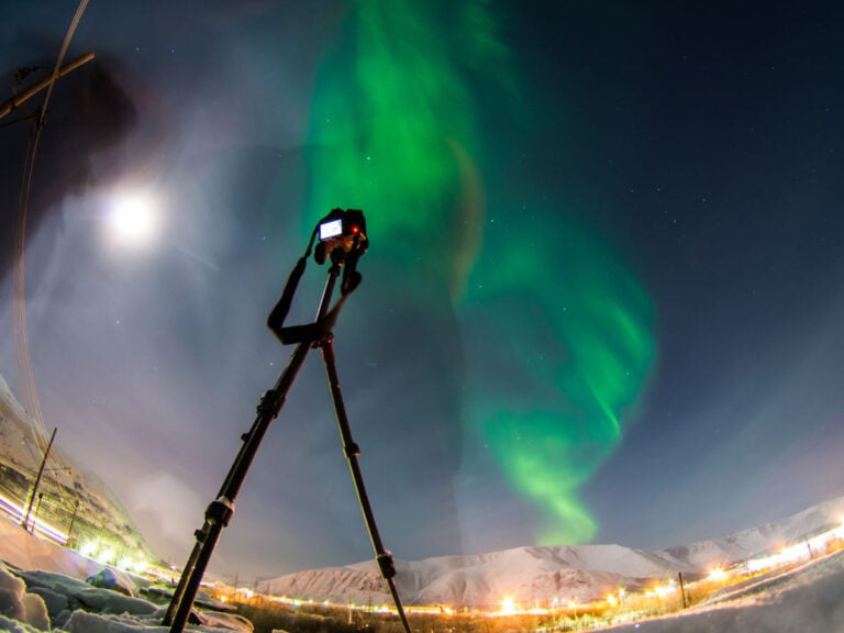 Camera on a tripod with the northern lights in the background.