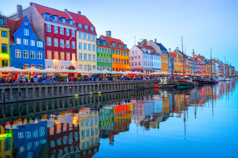 People walking and sitting in restaurants at illuminated Nyhavn in Copenhagen, Denmark.