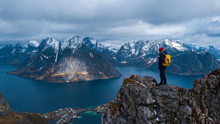 Norway's mountainous Lofoten Islands rising out of the sea with a hiker watching over the landscape.