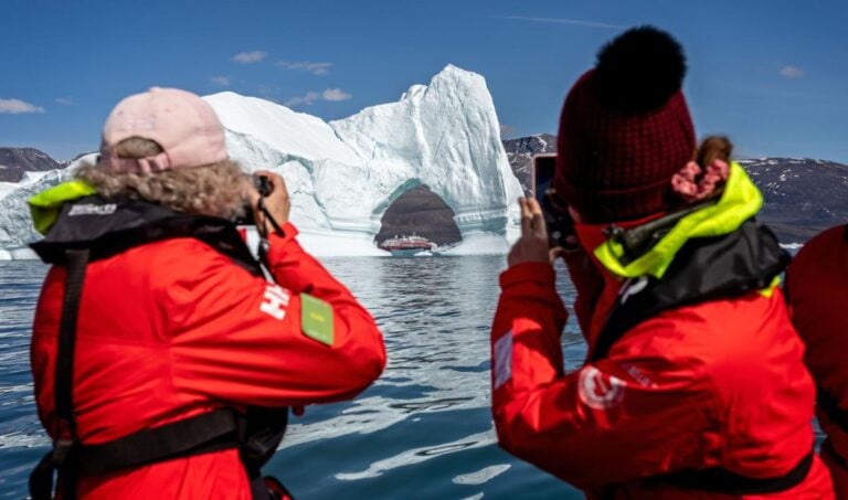 Hurtigruten passengers photographing the MS Fridtjof Nansen from a zodiac through an arch in a large iceberg at Disko Bay, Greenland. Photo: Nigel Jarvis / Shutterstock.com.