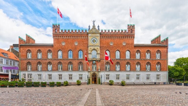 Historic building in Odense, Denmark, with Danish flags outside.